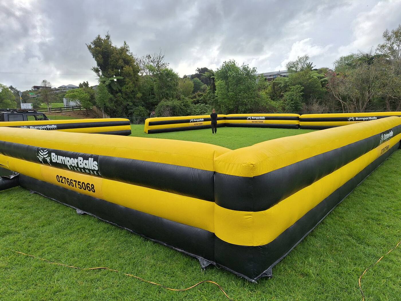 The yellow and black Bumper Balls Taranaki inflatable arena set up on grass